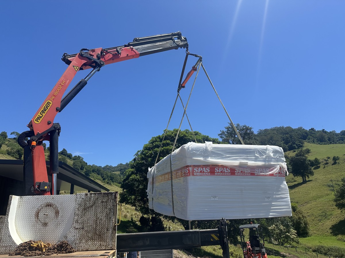 Crane truck lifting wrapped freight on a rural property