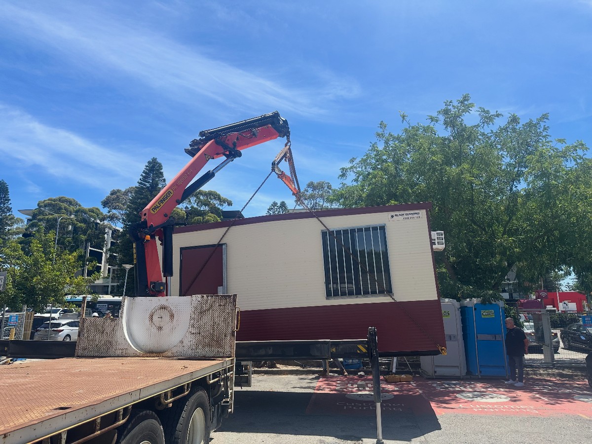 Crane truck relocating a site shed in a car park